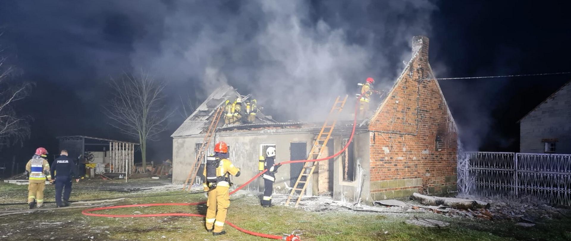 Noc strażacy prowadzą działania gaśnicze podczas pożaru budynku gospodarczego, część z nich znajduje się na stropie rozbierając i dogaszając spalony dach