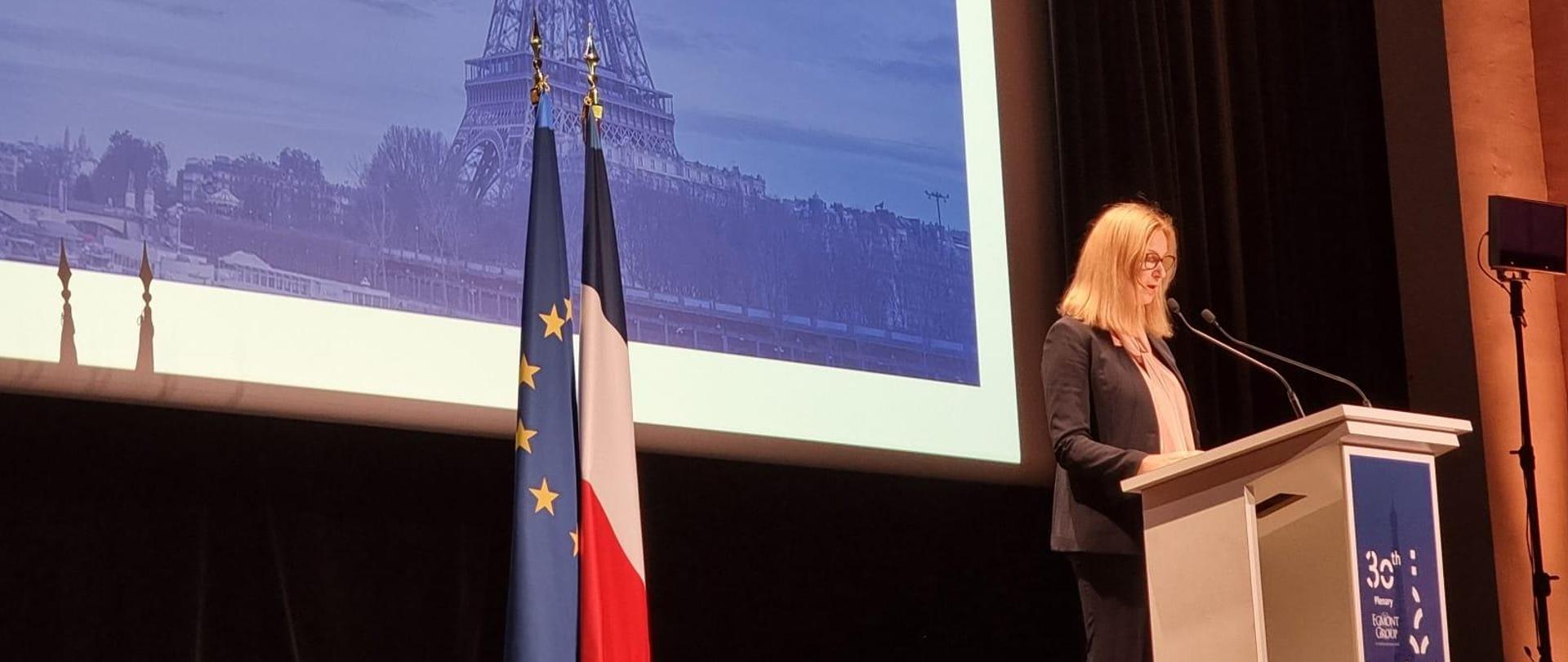 Elżbieta Franków-Jaśkiewicz przewodnicząca Grupy Egmont przemawia na mównicy, obok flaga Unii Europejskiej i Francji