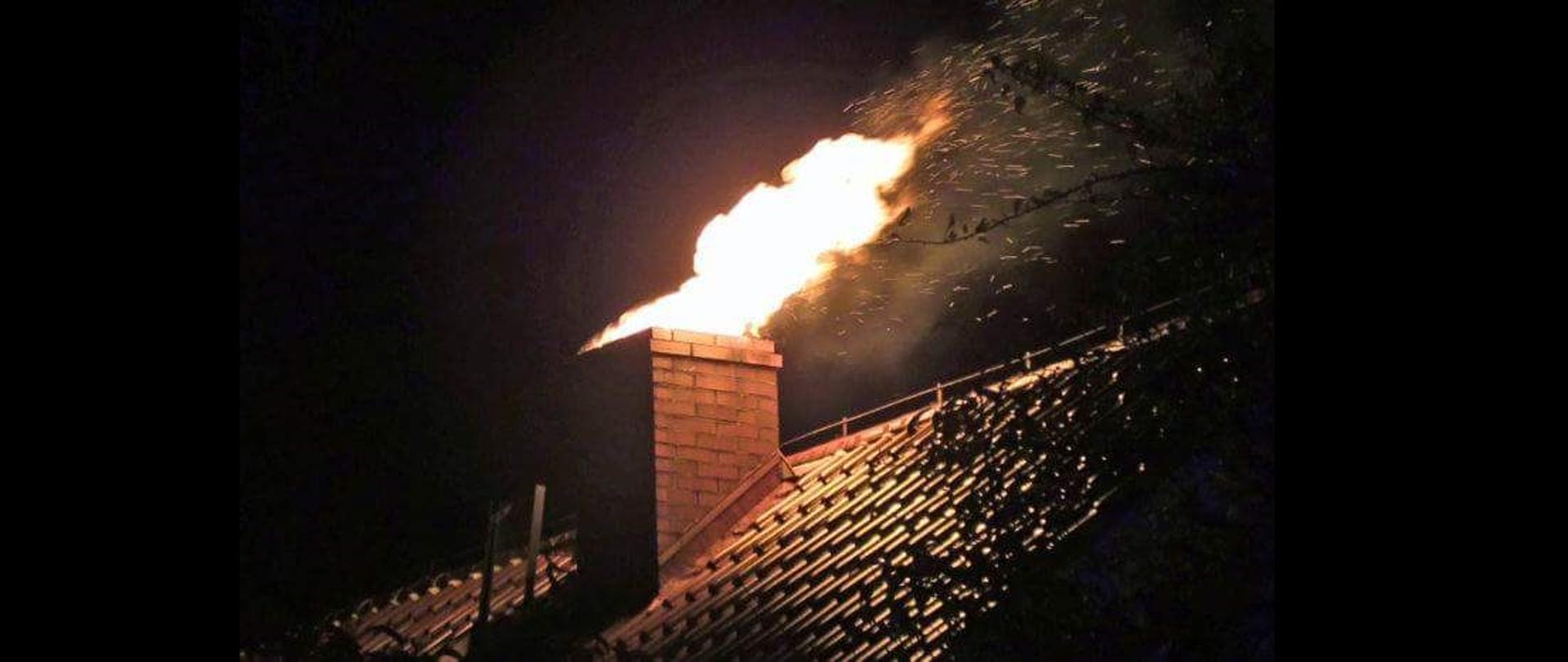Zdjęcie przedstawia płonący komin, z którego wylatują języki ognia oraz iskry. Zdjęcie wykomane nocą.