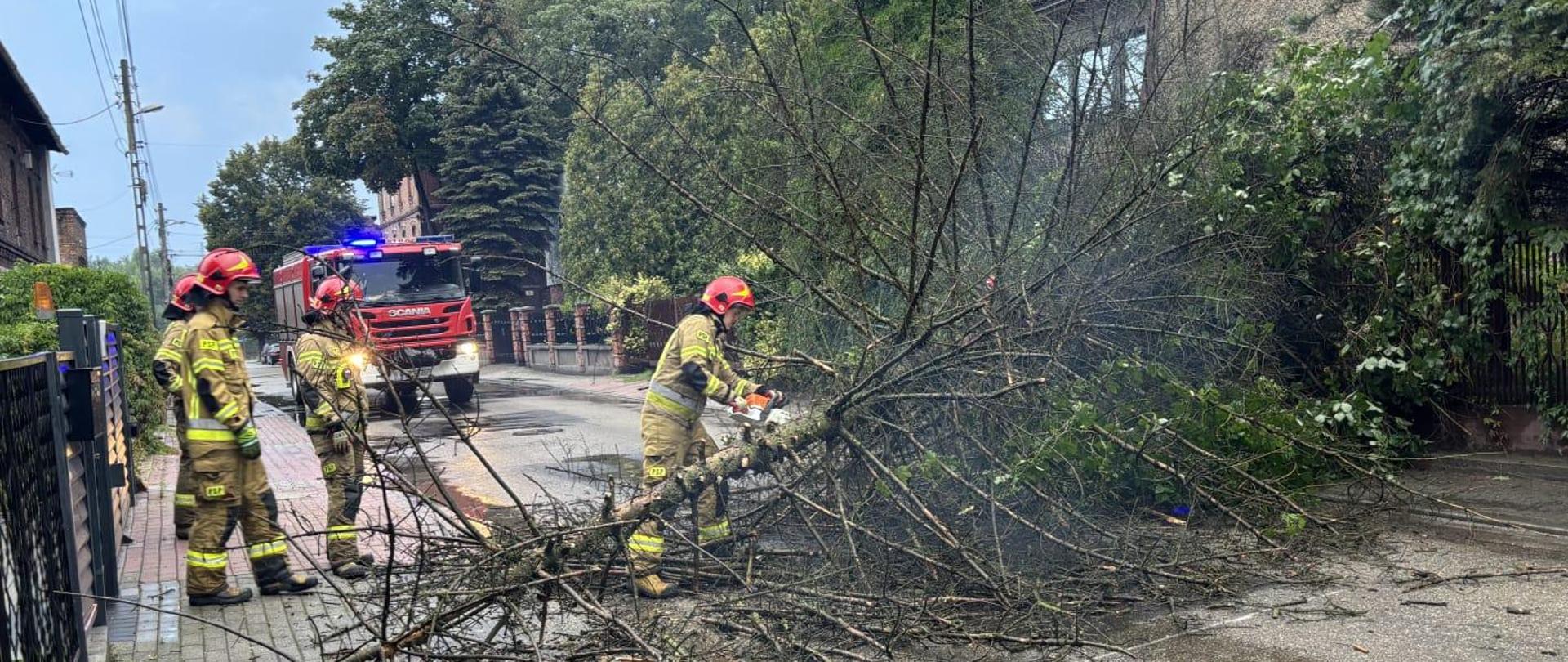 Strażak tnie drzewo przy użyciu piły mechanicznej.