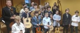 Wspólne zdjęcie połączonych klas gitar i kontrabasu wraz z nauczycielami w auli szkolnej.