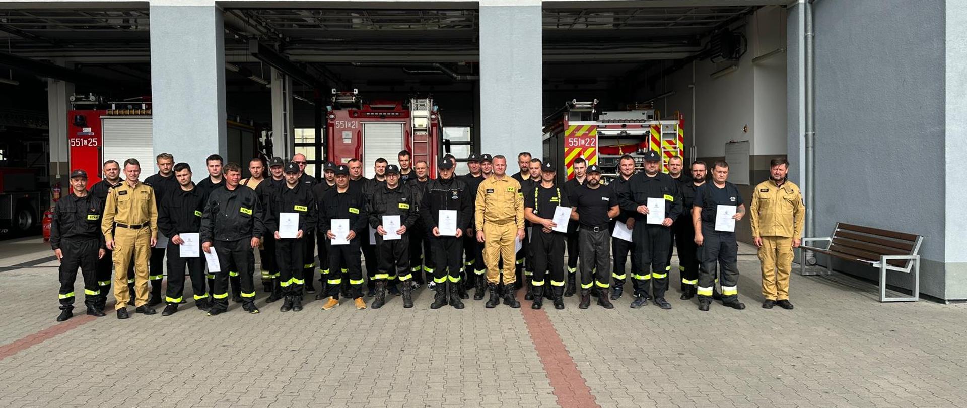 Egzamin podsumowujący szkolenie kierowców- konserwatorów sprzętu ratowniczego ochotniczych straży pożarnych. Zdjęcie wszystkich uczestników kursu na tle garaży podziału bojowego.