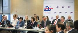 U szczytu stołu konferencyjnego na tle baneru z logo polskiej prezydencji siedzą w dwóch rzędach urzędnicy i słuchają wystąpień