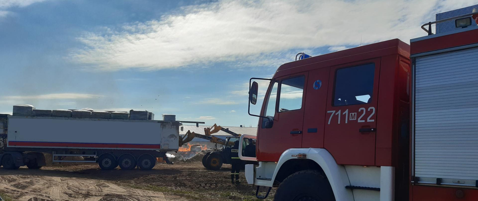 Samochód ratowniczo- gaśniczy, a w tle ładowarka wypakowująca z tira wytłaczanki do spalenia.