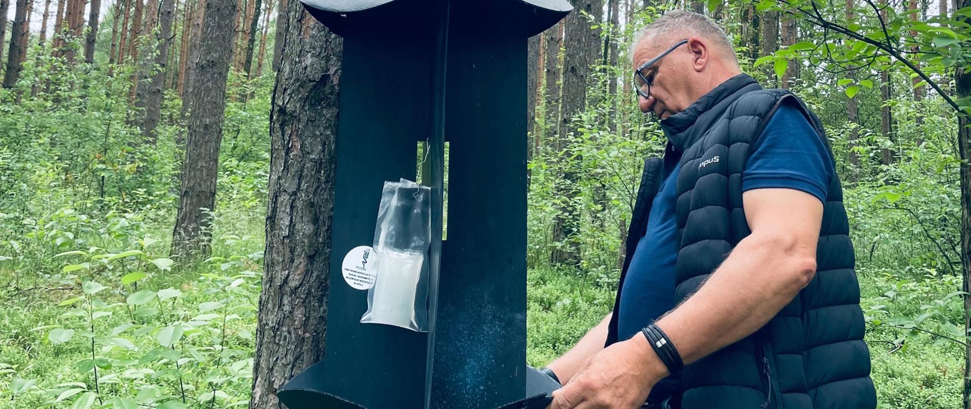 Zdjęcie przedstawia inspektora instalującego pułapkę w lesie