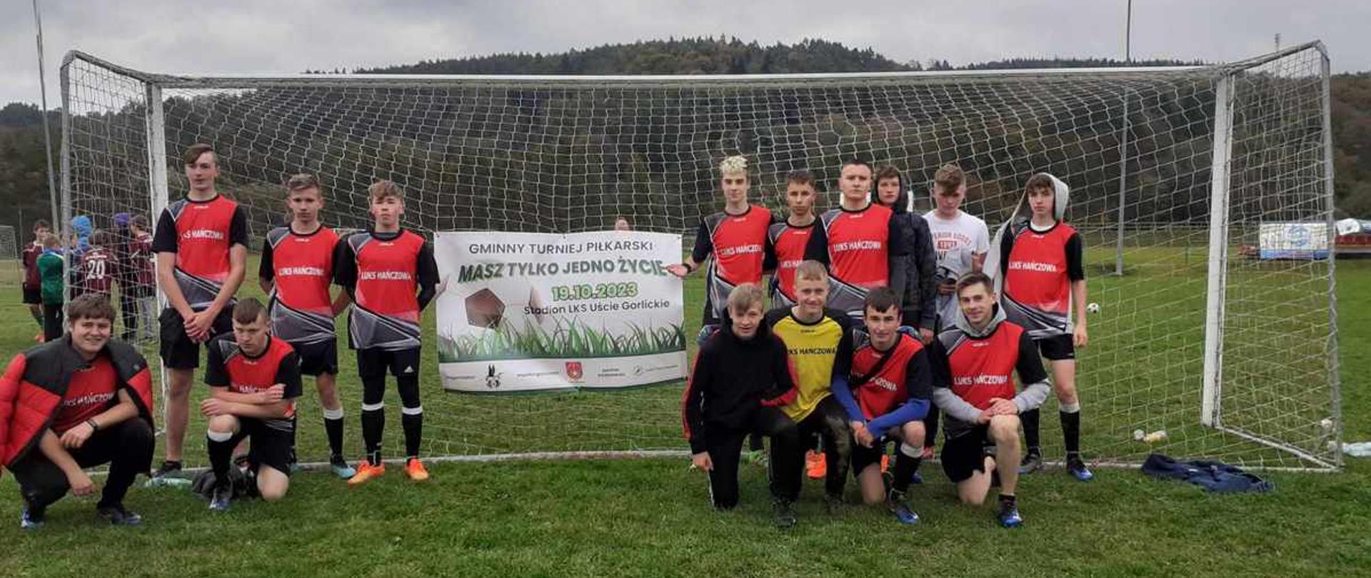 Drużyna LUKS Hańczowa w czerwono-czarnych strojach pozuje pod bramką z banerem turnieju "Masz tylko jedno życie".