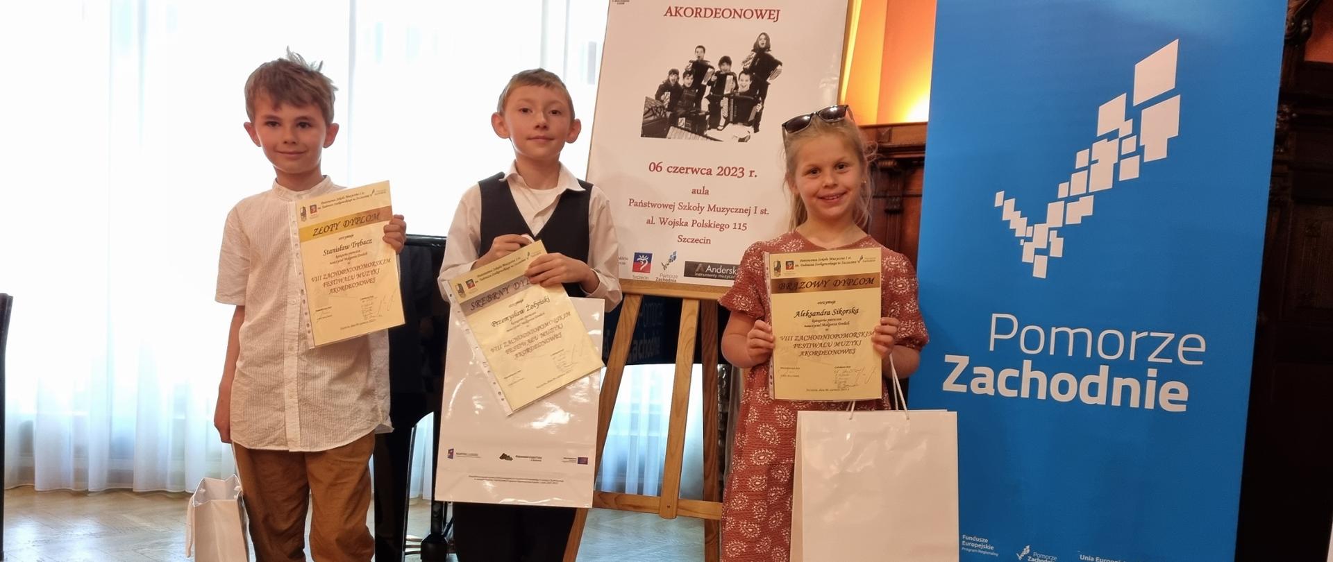 Na scenie, na tle plakatu konkursowego troje uczniów