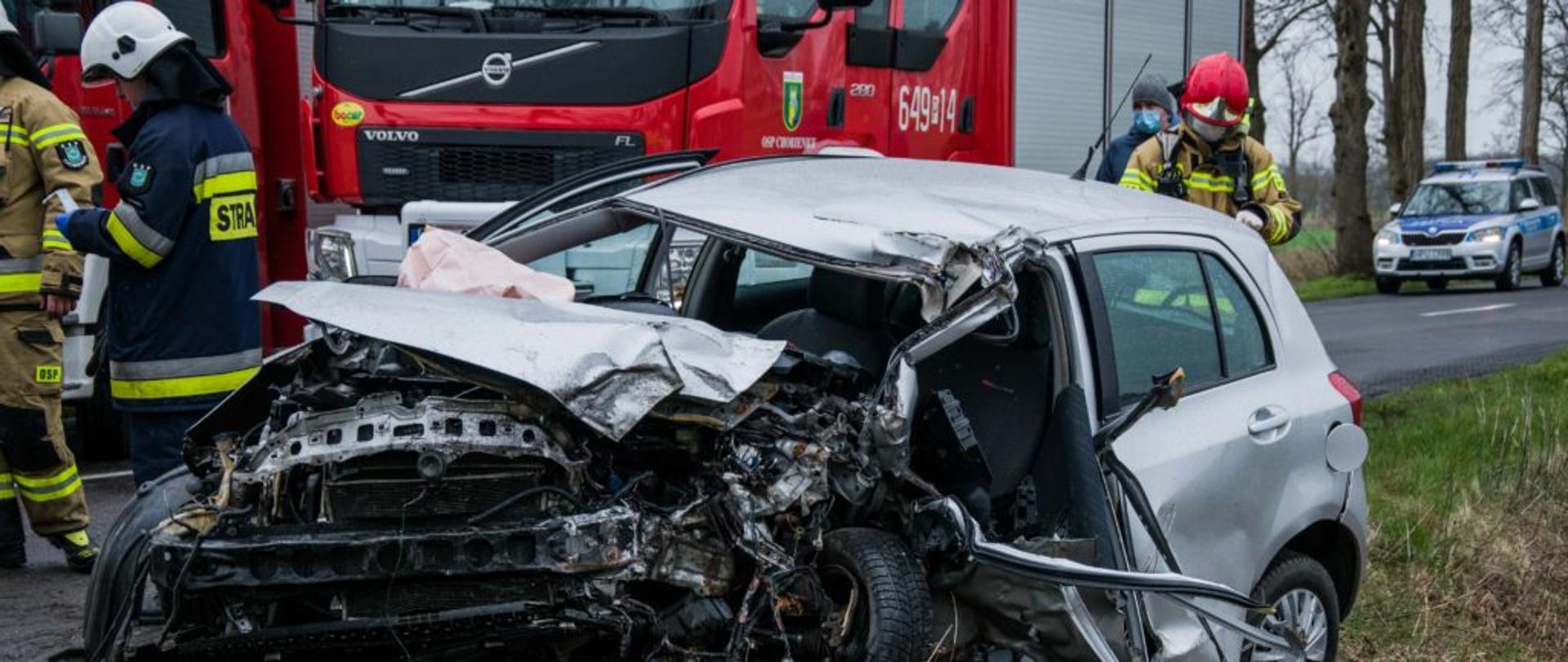 Rozbity samochód, z tyłu samochód strażacki, dookoła strażacy.