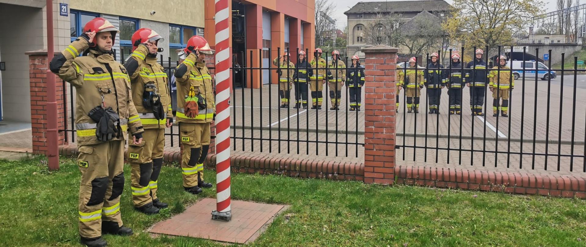 Poczet flagowy salutuje pod masztem, w tle zmiana służbowa, wszyscy w ubraniach specjalnych