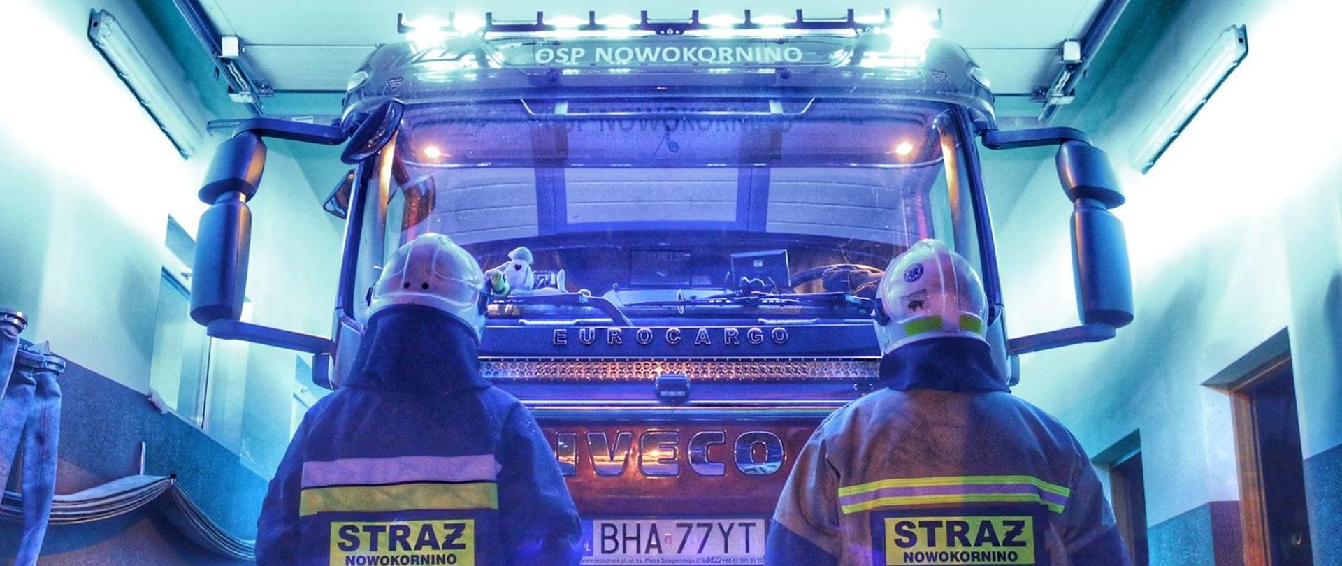 Na tle samochodu z napisem OSP Nowokornino tyłem stoi dwóch strażaków w ubraniach specjalnych.