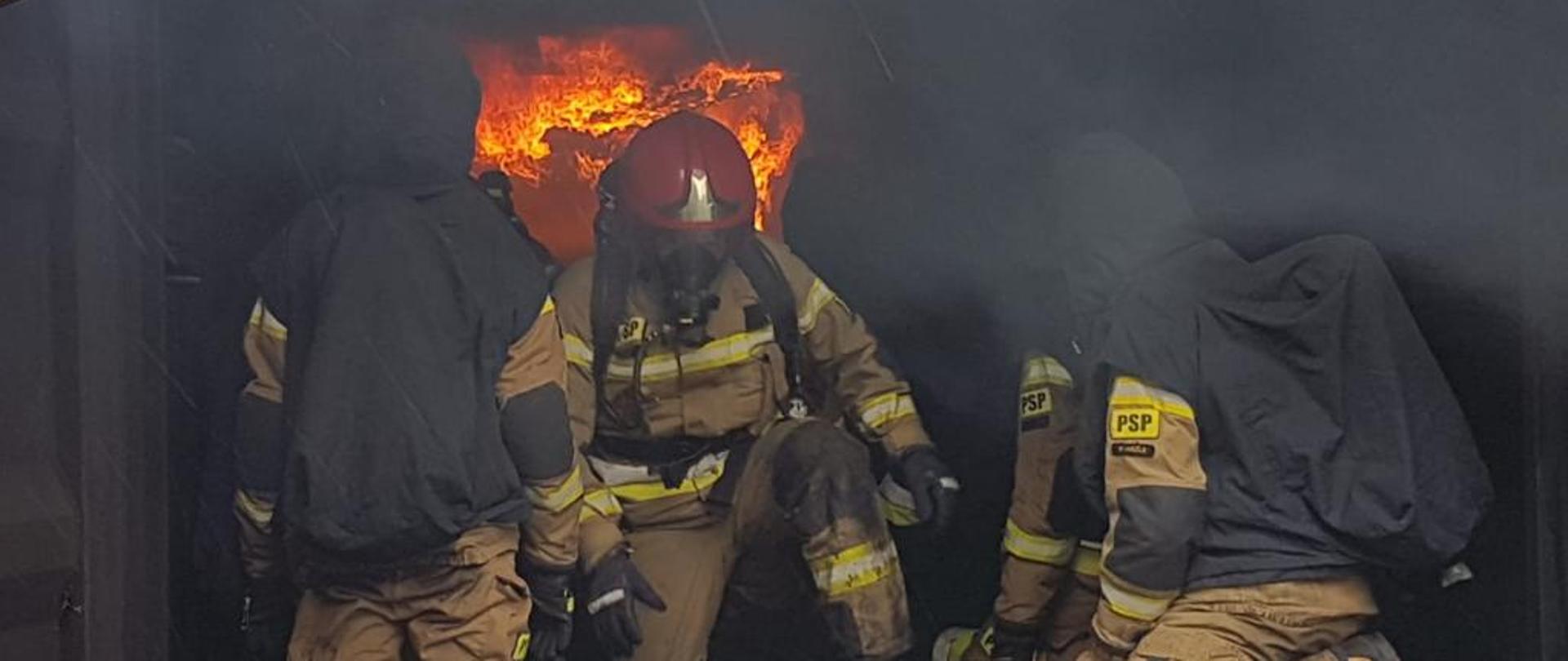 Strażacy zabezpieczeni w sprzęt ochronny ćwiczą w komorze rozgorzeniowej. 