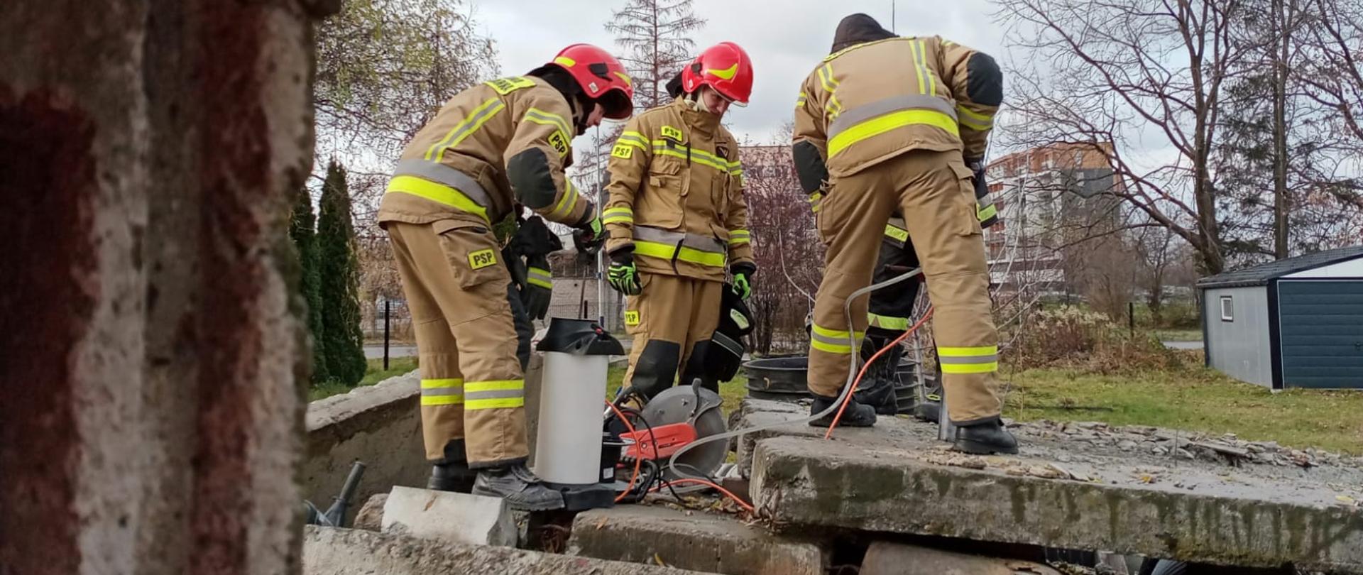 Strażacy wykonujący przebicia w ścianie w trakcie szkolenia z działań poszukiwawczo-ratowniczych realizowanych przez KSRG w zakresie podstawowym