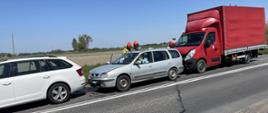 Zdjęcie przedstawia trzy samochody na drodze biały srebrny oraz czerwony dostawczak przy srebrnym stoi dwóch strażaków