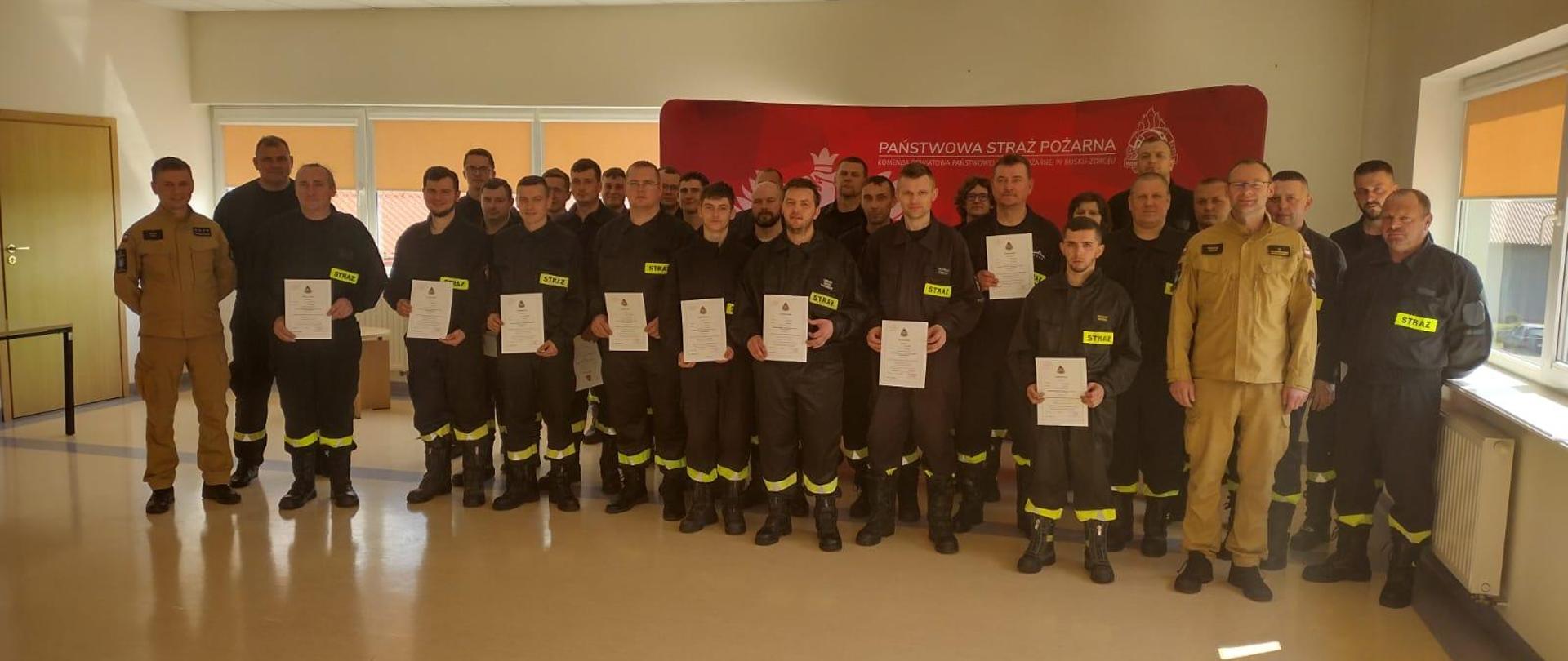 Zdjęcie grupowe strażaków biorących udział w szkoleniu. W tle napis Państwowa straż pożarna.