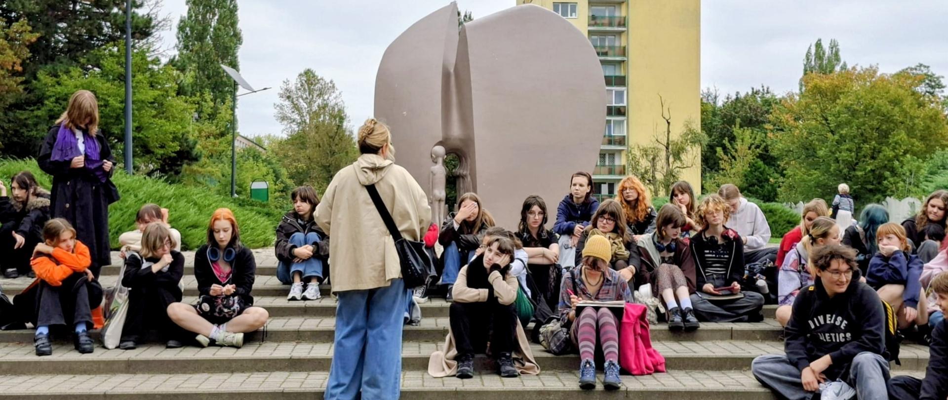 Na zdjęciu uczniowie siedzą na schodach przy Pomniku Martyrologii Dzieci „Pękniętego Serca”