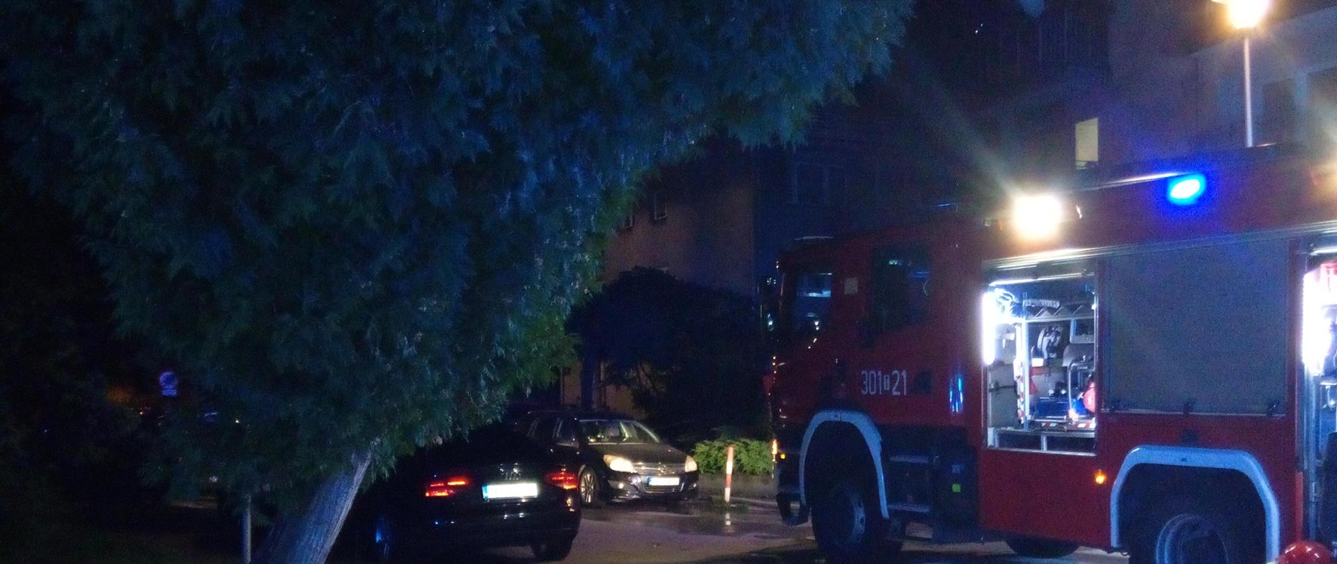 Zdjęcie przedstawia ulicę Zagórską. Po prawej stronie stoi wóz strażacki, a za nim widać fragment budynku wielorodzinnego gdzie wybuchł pożar.