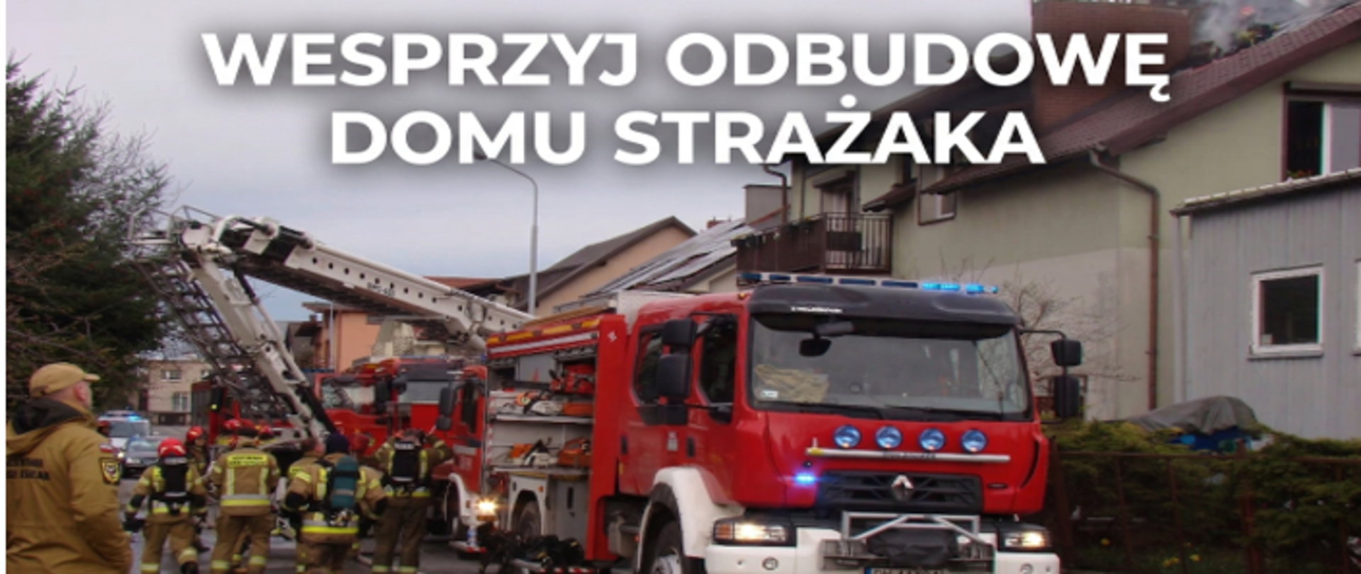 Grafika o charakterze charytatywnym. U góry widnieje duży, biały napis: „WESPRZYJ ODBUDOWĘ DOMU STRAŻAKA”. W tle znajduje się zdjęcie z prawdziwej akcji: na pierwszym planie stoi wóz strażacki z włączonymi niebieskimi sygnałami świetlnymi, obok pracują strażacy w pełnym umundurowaniu bojowym, a w głębi widać rozłożony podnośnik hydrauliczny skierowany w stronę dachu budynku jednorodzinnego.