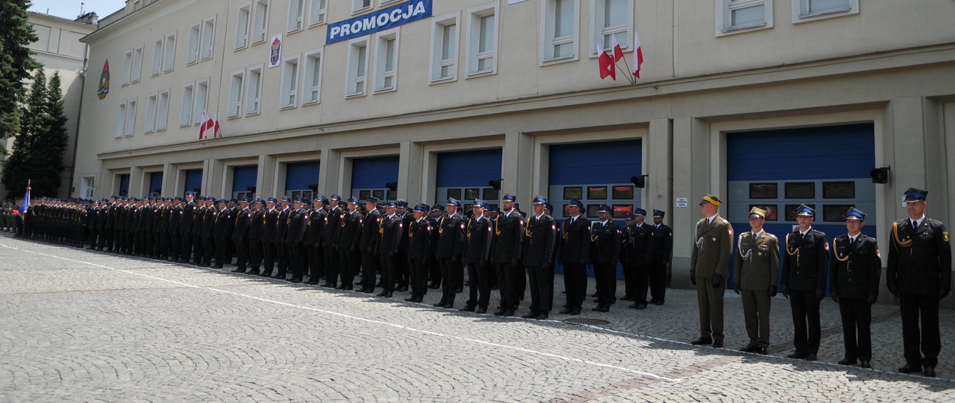 Funkcjonariusze w ubraniach wyjściowych stojący w na tle szkoły podczas promocji