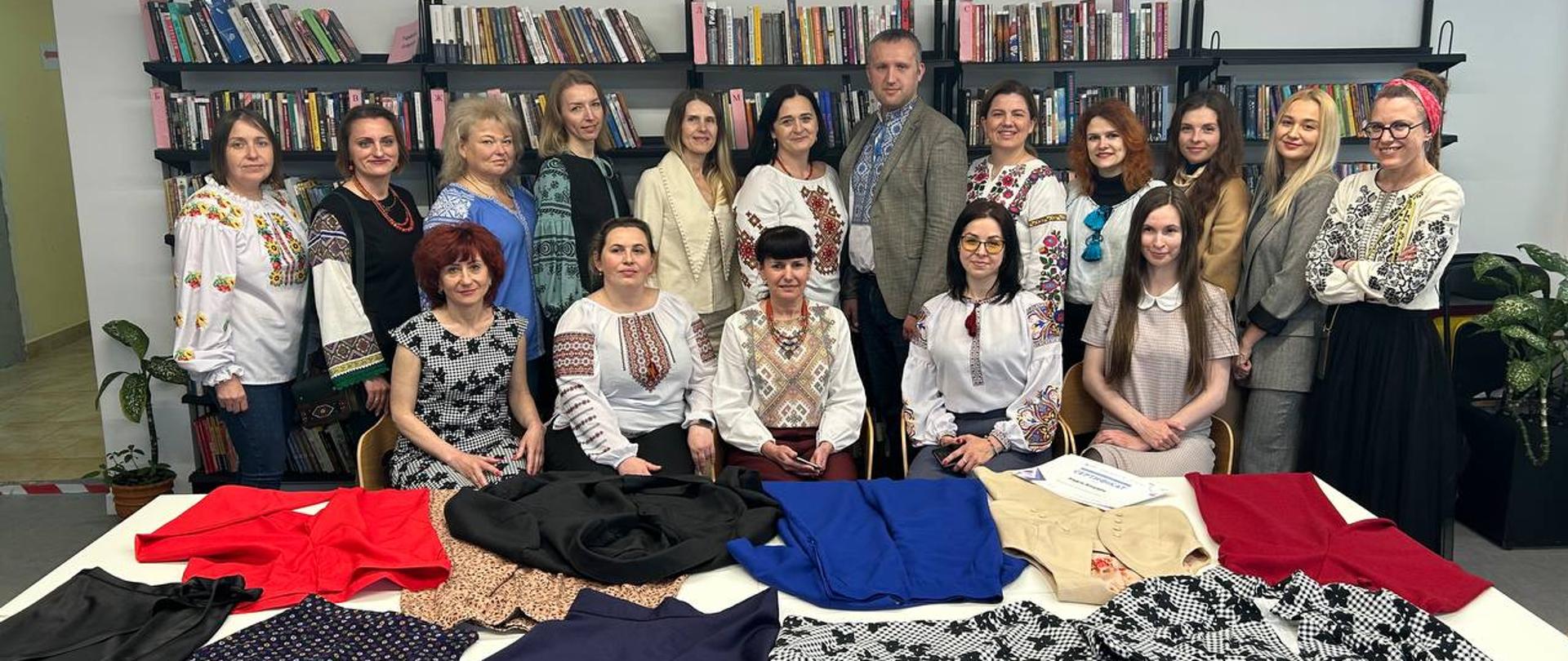 Grupa kobiet i mężczyzna pozują do zdjęcia przed stołem, na którym rozłożone są ubrania.