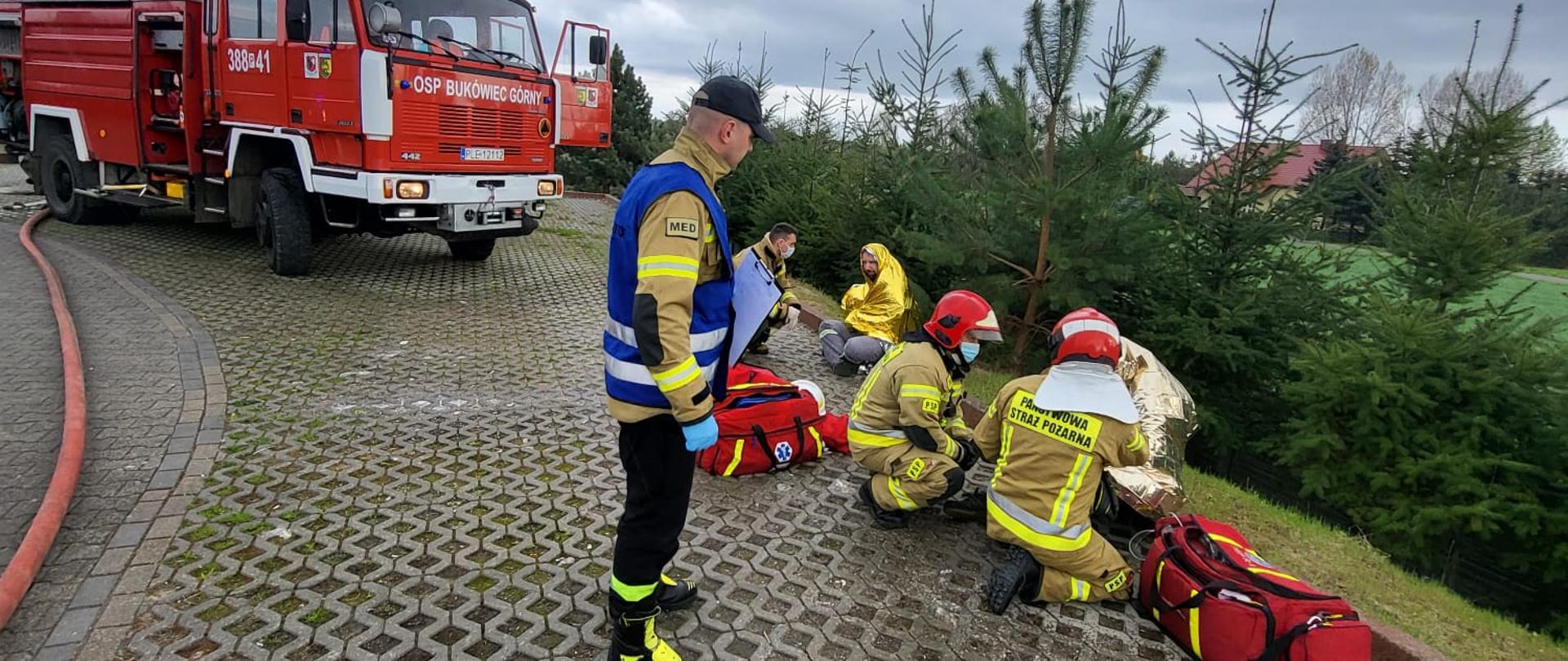 Strażacy udzielają pomocy osobą poszkodowanym na zewnątrz.