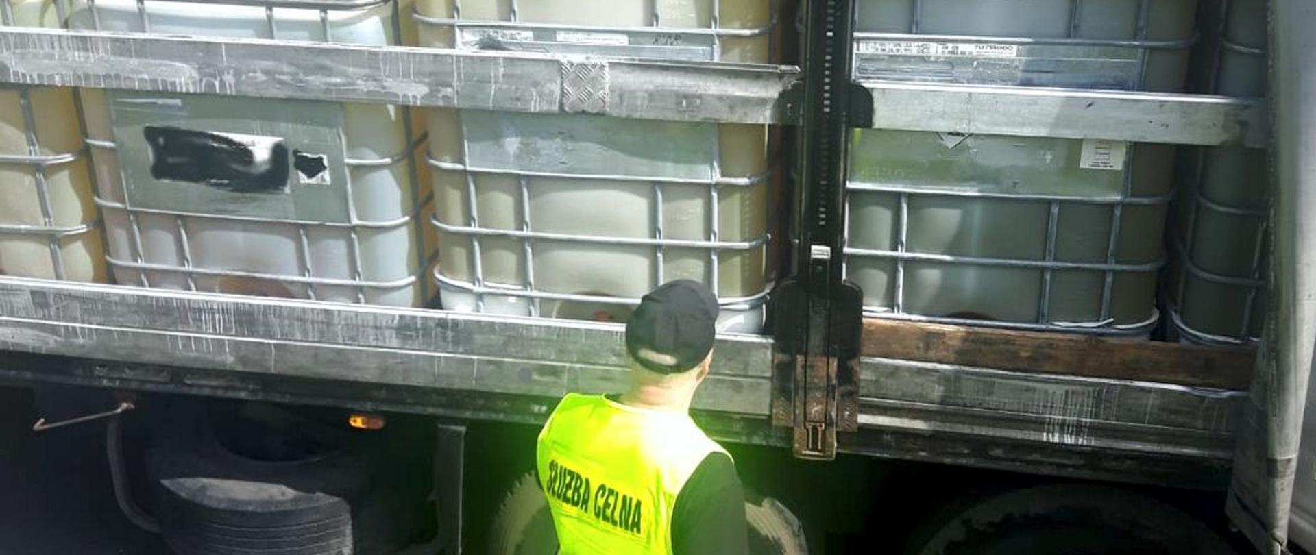 Funkcjonariusz Służby Celno-Skarbowej KAS przed otwartym bokiem naczepy z pojemnikami z substancją ropopochodną.
