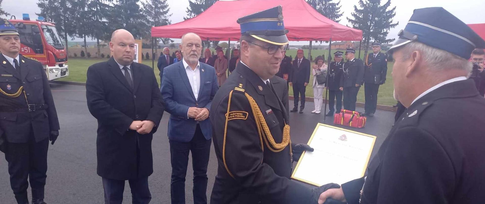 Zastępca Wielkopolskiego Komendanta Wojewódzkiego wręcza akt włączenia do KSRG. W tle stoją parlamentarzyści.