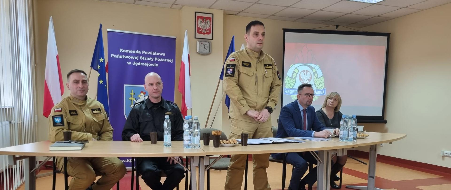 Przy stole prezydialnym widać od lewej zastępcę komendanta powiatowego PSP w Jędrzejowie bryg. Tomasza Szymańskiego, komendanta powiatowego PSP w Jędrzejowie mł. bryg. Mariusza Stolarczyka, świętokrzyskiego komendanta wojewódzkiego PSP w Kielcach nadbryg. Krzysztofa Cioska, który przemawia na stojąco, starostę jędrzejowskiego i wicestarostę. 