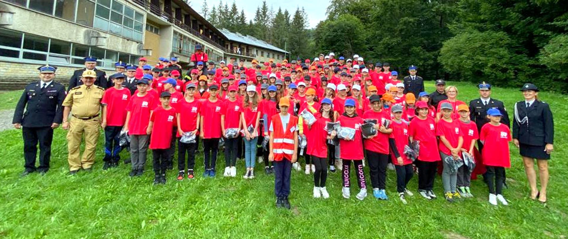 Zdjęcie zrobione na zewnątrz podczas uroczystej zbiórki uczestników obozu Młodzieżowych Drużyn Pożarniczych. Zdjęcie grupowe. Na zdjęciu uczestnicy obozu wraz z kadrą.