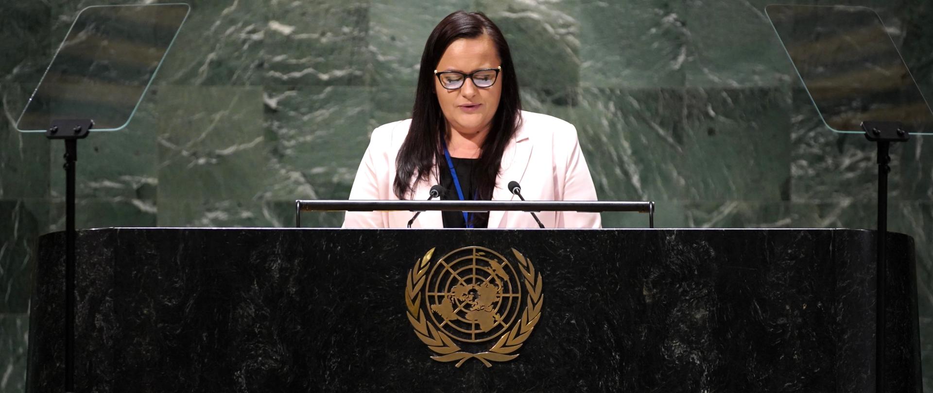 Na zdjęciu wiceminister Małgorzata Jarosińska-Jedynak stojąca przy mównicy i przemawiająca. Na mównicy logo ONZ. W tle dwoje ludzi siedzących powyżej.