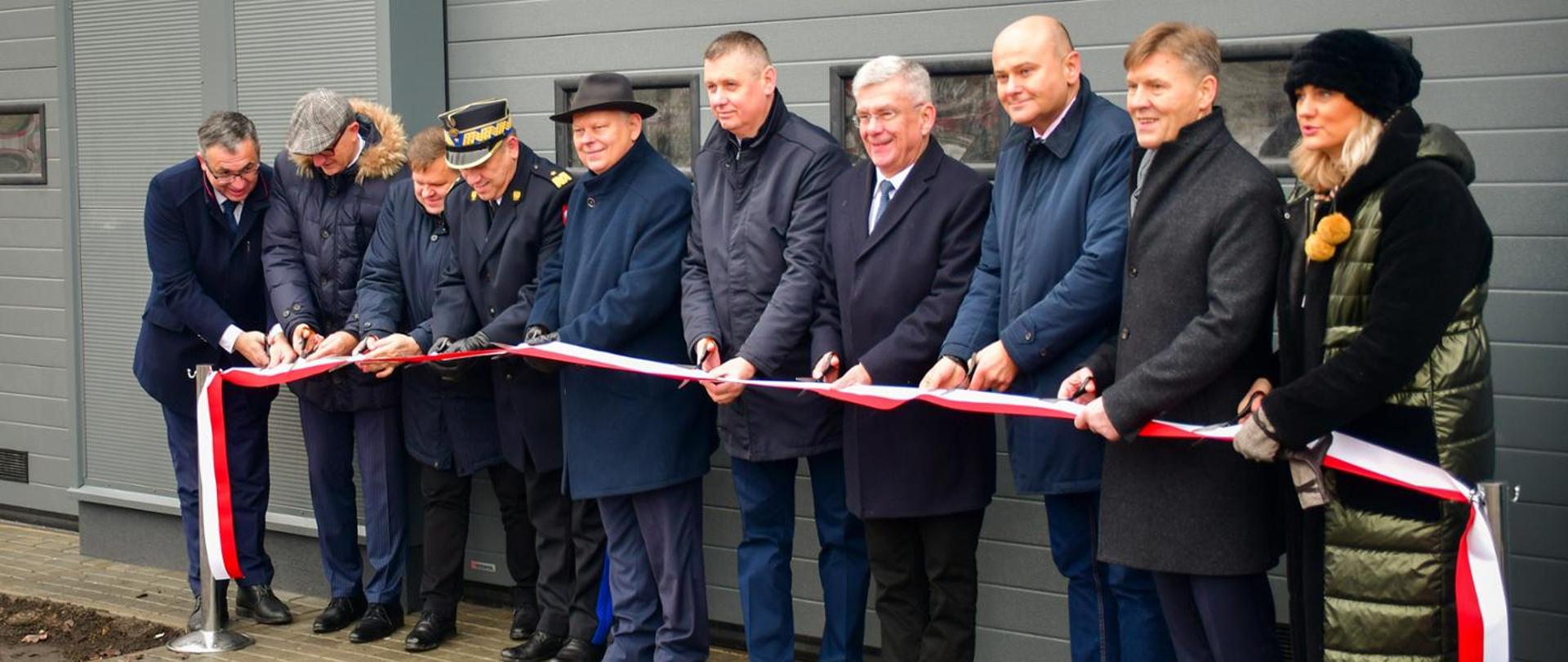 Fotografia przedstawiająca przecięcie wstęgi przez gości zaproszonych podczas uroczystości włączenie jednostek Ochotniczych Straży Pożarnych do Krajowego Systemu Ratowniczo-Gaśniczego