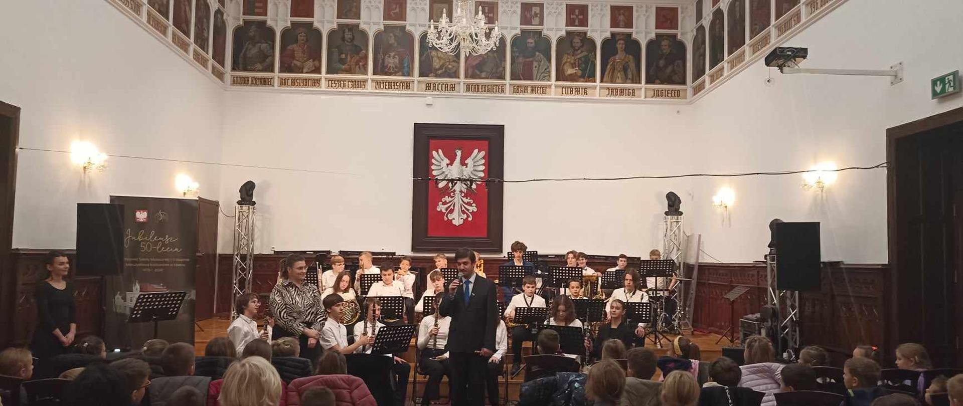 Piotr Rysiewicz i orkiestra dęta I st. podczas audycji dla najmłodszych w Sali królewskiej psm mielec
