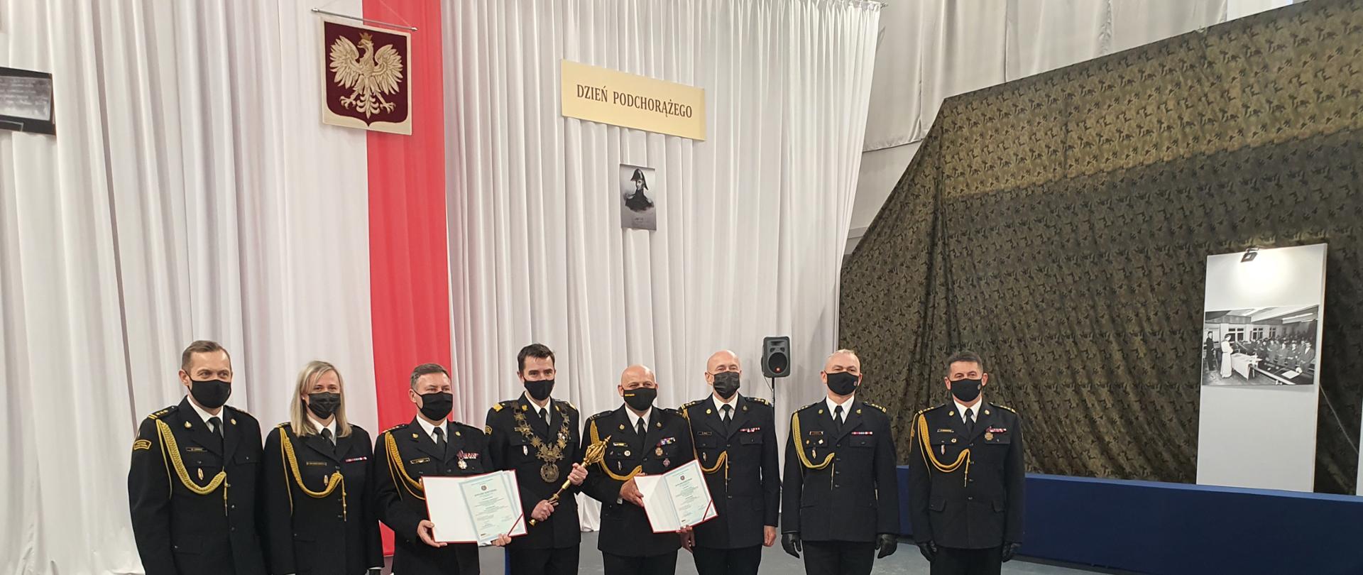 Zdjęcie przedstawia dwóch oficerów PSP z dyplomami doktorskimi oraz kadrę kierowniczą Szkoły Głównej Służby Pożarniczej w Warszawie.