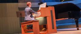 Mężczyzna gra na organach siedząc tyłem do publiczności na scenie sali koncertowej PSM.