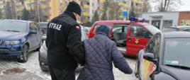 Strażak OSP prowadzi starsza panią do samochodu strażackiego
