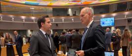 Dwóch mężczyzn stoi i rozmawia w okrągłej sali konferencyjnej. Jednym z nich jest Podsekretarz Stanu Wojciech Zajączkowski