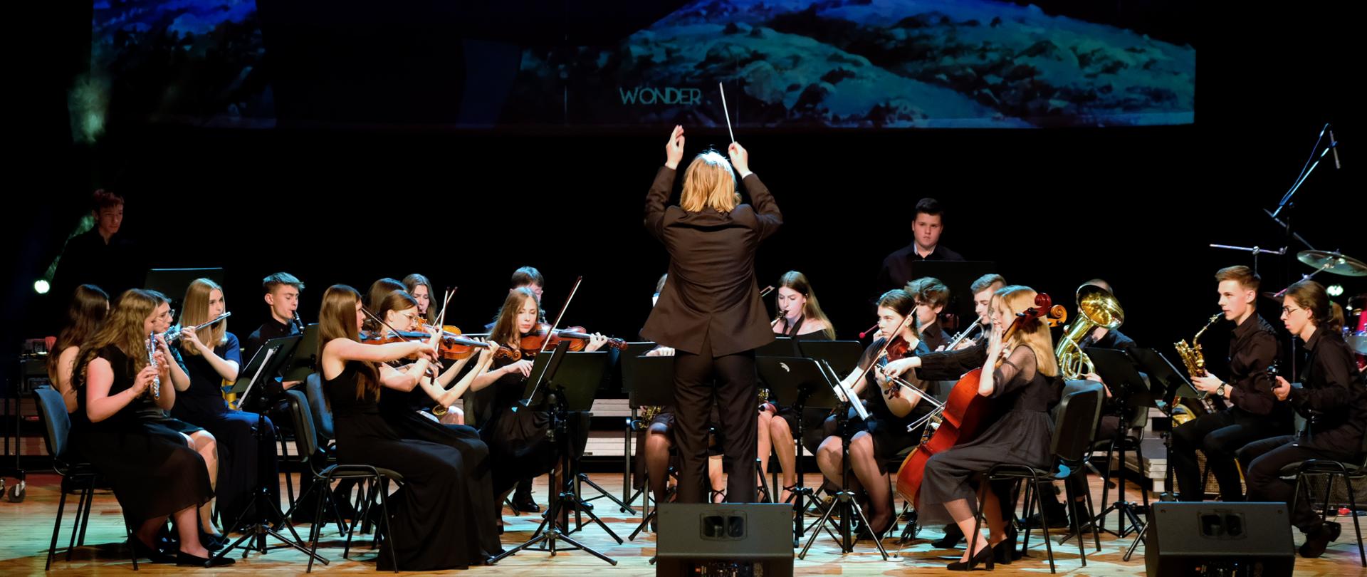 Muzycy orkiestrowi grający na tle ekranu z kadrem filmowym na scenie RCKP w Krośnie
