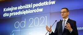 Premier na tle prezentacji dot. obniżek podatków dla przedsiębiorców.