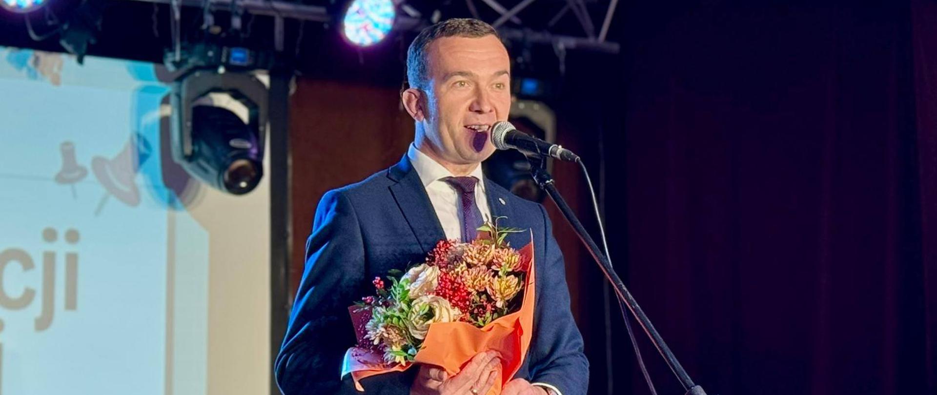 Mężczyzna stoi na scenie z kwiatami w ręku 