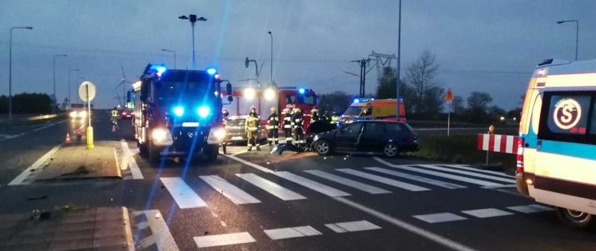 Widok ogólny na miejsce zdarzenia. Skrzyżowanie ulic, widać auta ratownicze i auta uczestniczące w zdarzeniu. Zdjęcie wykonane o świcie. Jest jeszcze szaro, wstaje dzień.