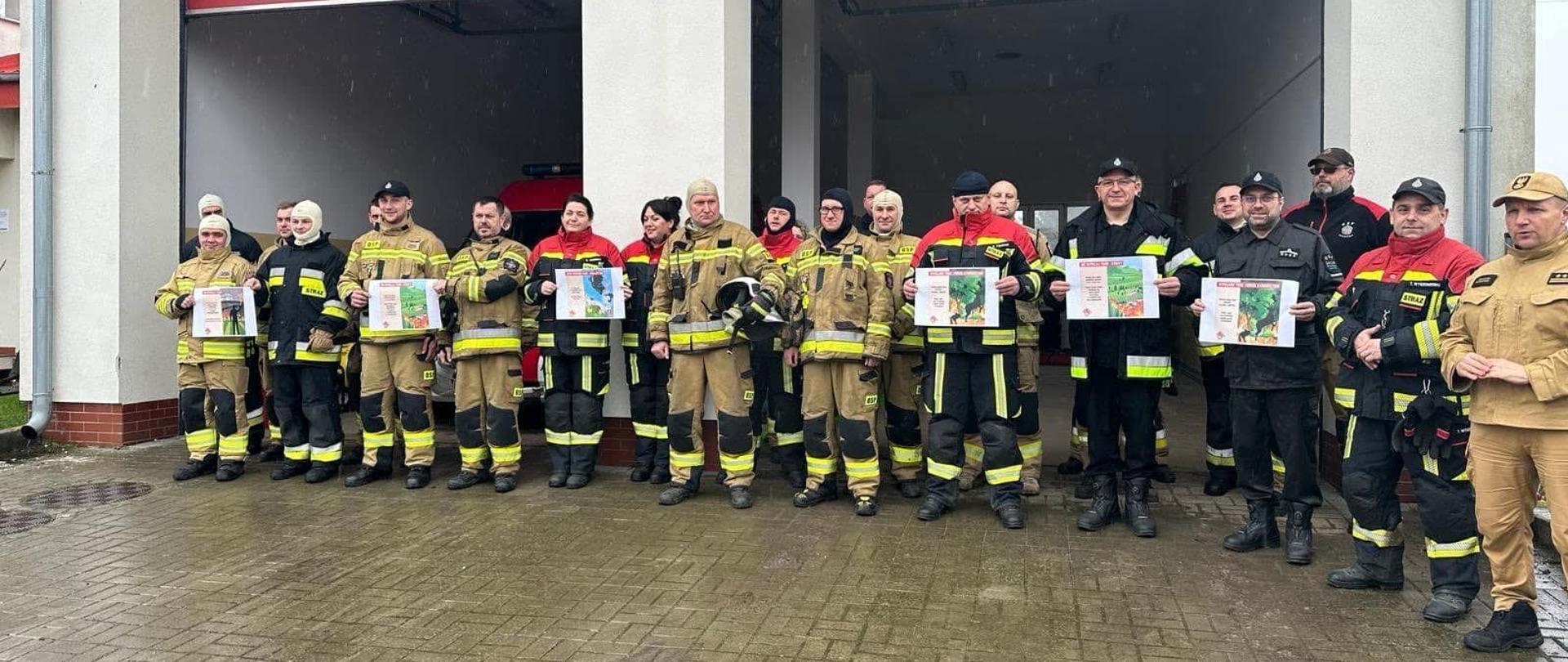 Przy strażnicy stoi duża grupa strażaków w mundurach.
