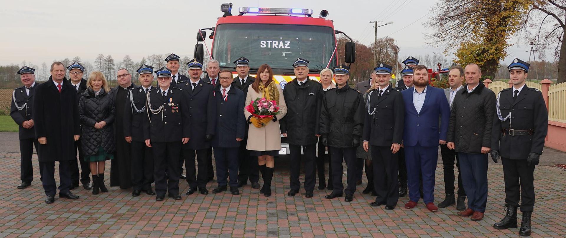 uczestnicy uroczystości pozują do zdjęcia przed samochodem ratowniczo-gaśniczym, strażacy PSP i druhowie OSP, poseł RP, przedstawiciele władz samorządowych