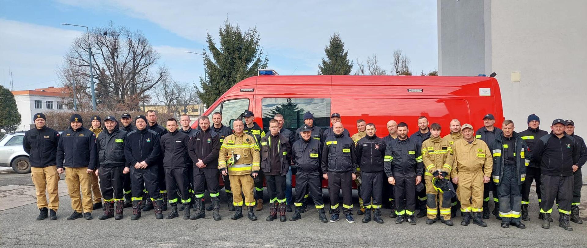 Strażacy stoją na tle pojazdu pożarniczego i pozują do zdjęcia grupowego. 