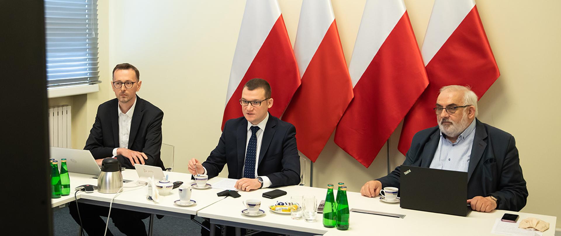 Posiedzenie KWRiST w formie wideokonferencji. Na zdjęciu za stołem siedzi Paweł Szefernaker Sekretarz Stanu MSWiA, Szymon Wróbel Zastępca Dyrektora DAP Sekretarz Strony Rządowej i Andrzej Porawski Sekretarz Strony Samorządowej