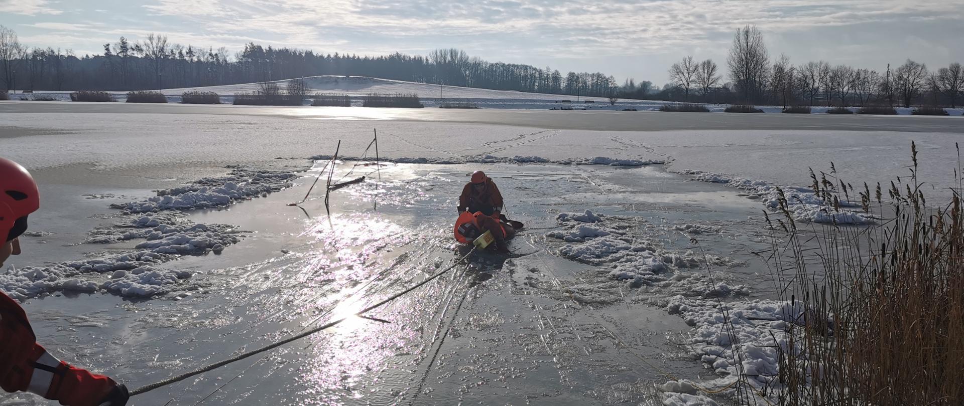 Na zdjęciu widoczni strażacy podczas szkolenia z ratownictwa lodowego na zbiorniku Kępina. Na zamarzniętym zbiorniku wycięty jest przerębel, w którym była osoba poszkodowana. Dwóch ratowników przy pomocy węgorza ratowniczego wyciąga poszkodowaną osobę z wody. . 