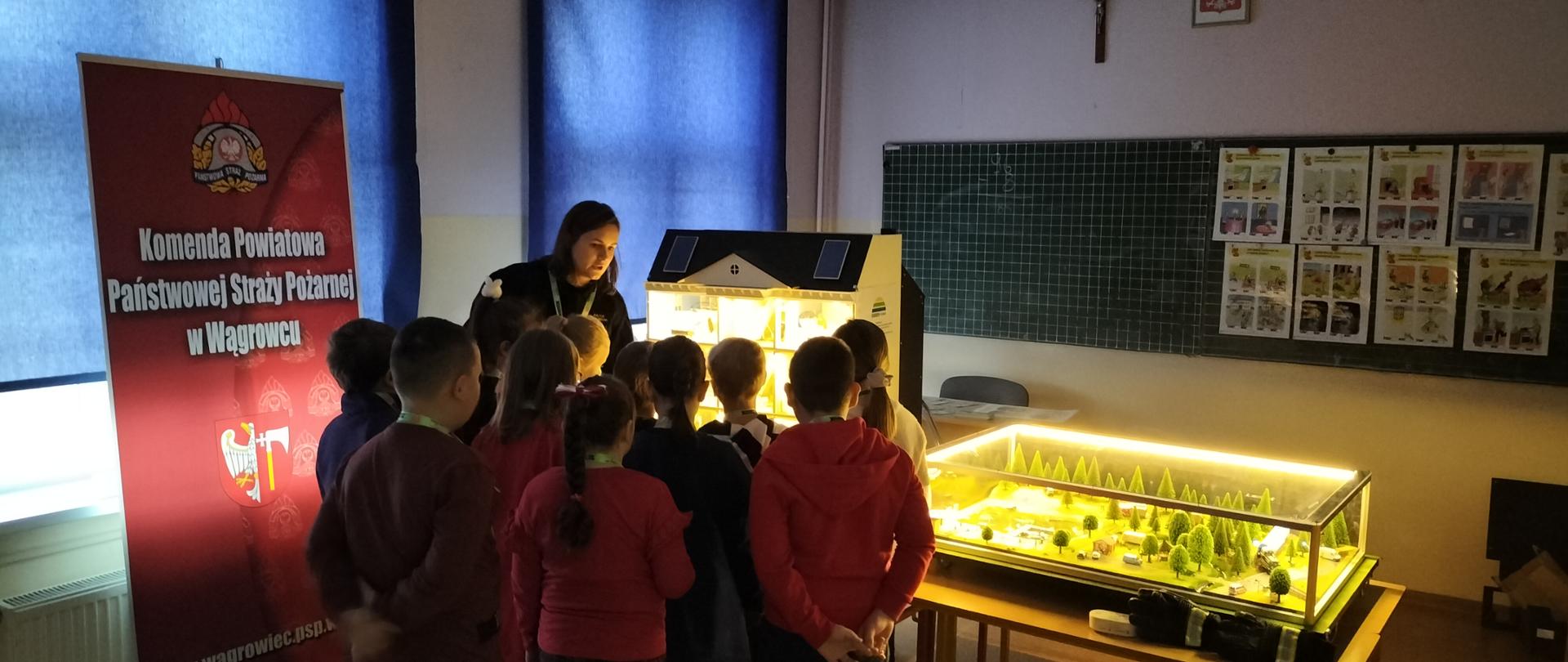 Na zdjęciu widać funkcjonariuszkę PSP oraz dzieci w trakcie przedstawiania zagadnień prewencyjnych 