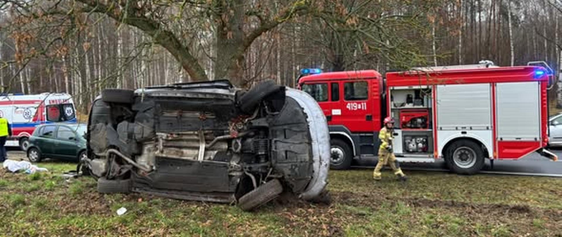 samochód osobowy na boku, w tle wóz strażacki oraz karetka