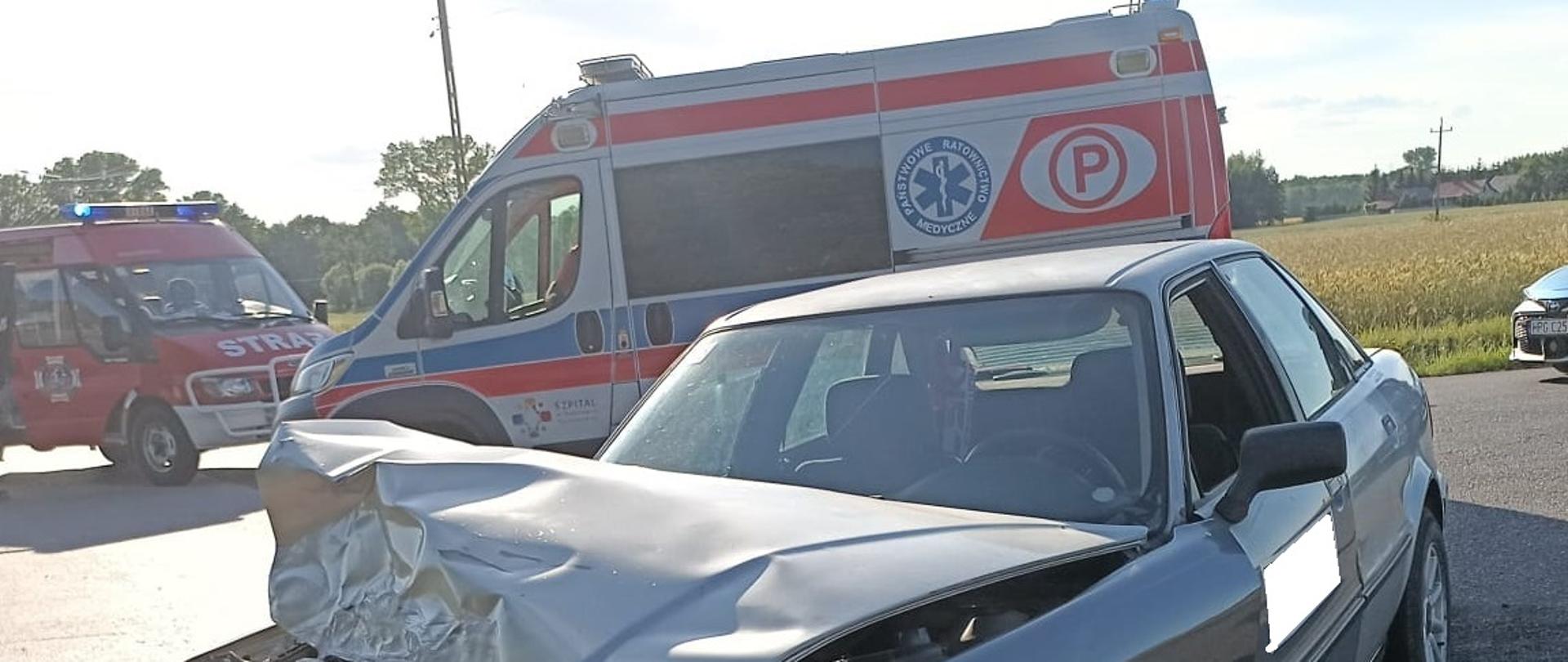 Na zdjęciu widać uszkodzony samochód osobowy , rozlane płyny eksploatacyjne, za pojazdem Zespół Ratownictwa medycznego i pojazdy Straży Pożarnej.