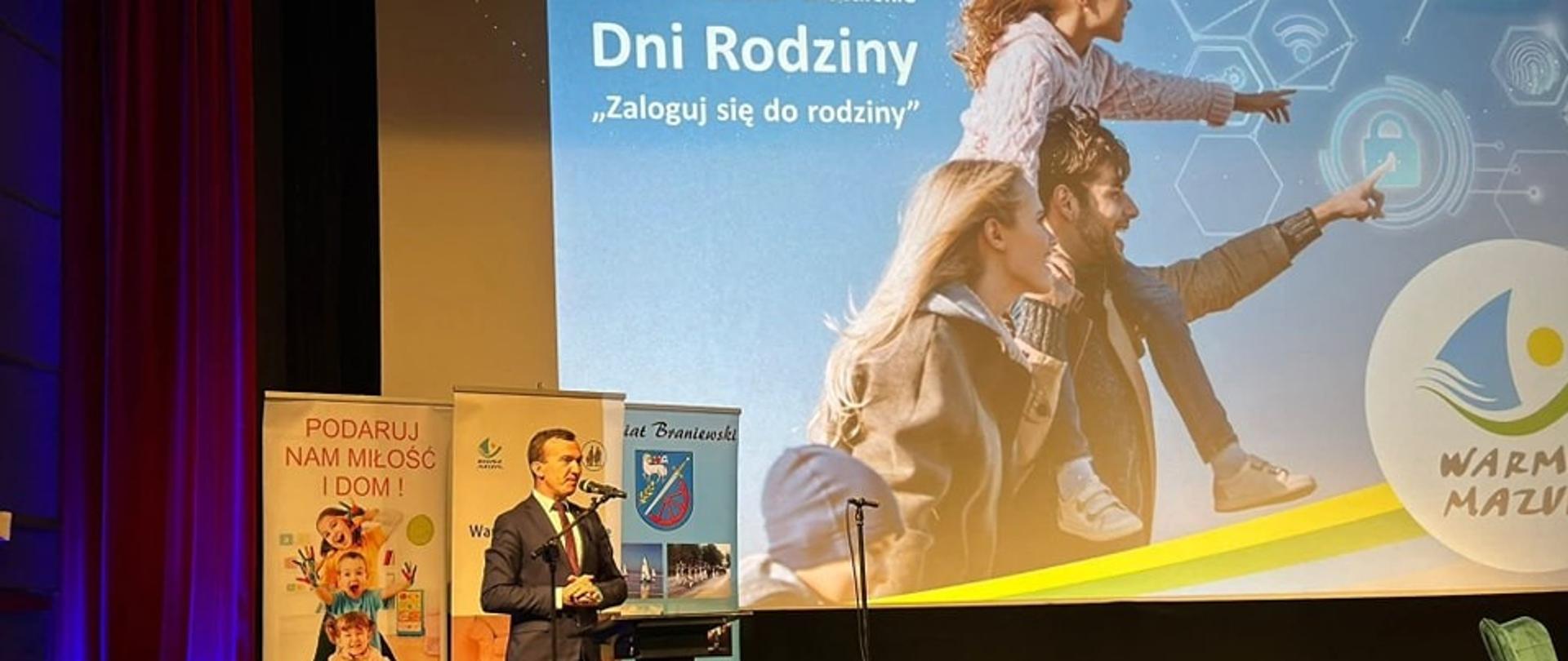 Wicewojewoda Mateusz Szauer stoi na scenie i przemawia przez mikrofon a w tle za nim na ekranie wyświetla się rodzina i napis "Dni Rodziny"