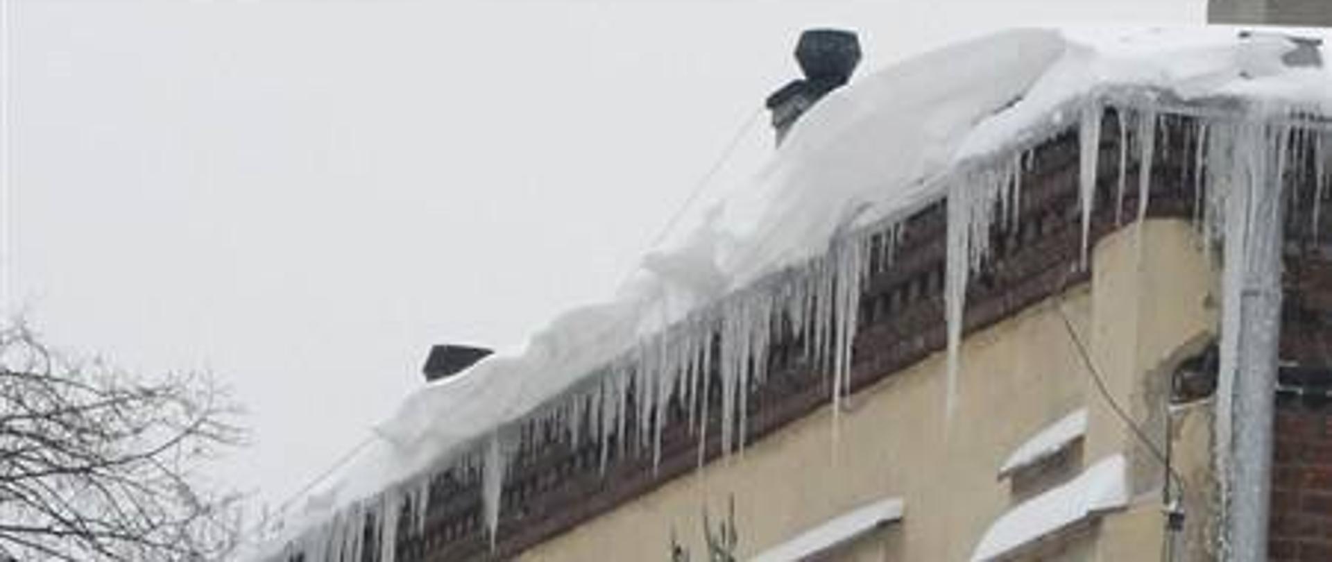 Baner przedstawiający dach z nawisam śnieżnymi i soplami lodu