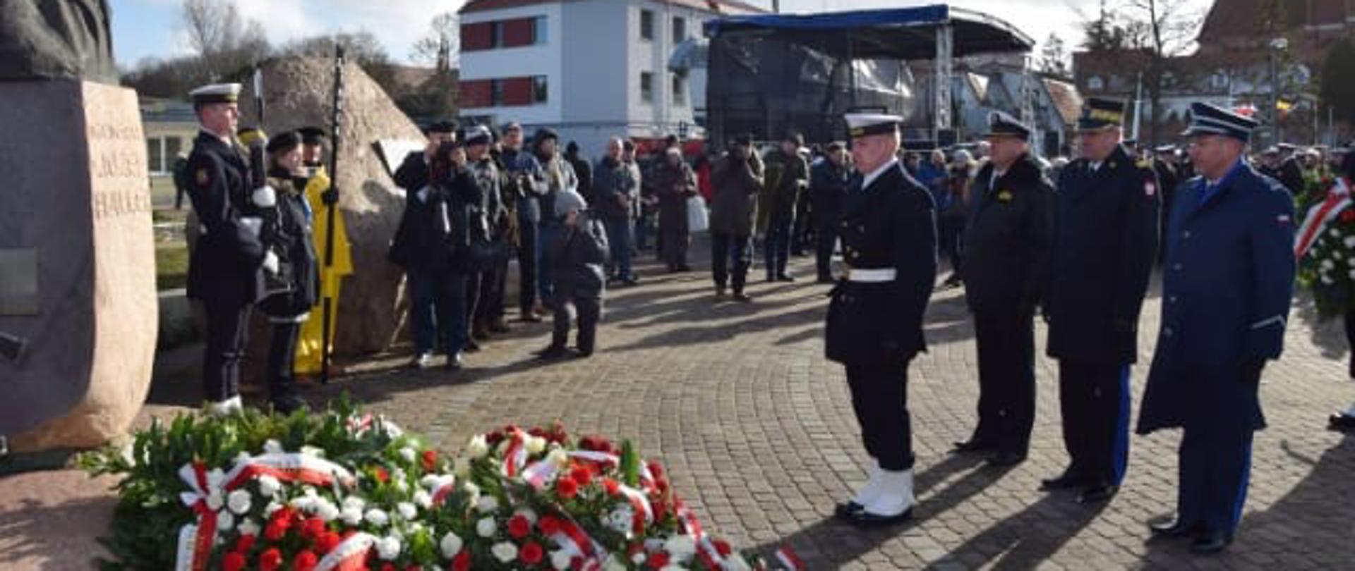 Wieńce leżą pod pomnikiem przed którym stoi żołnierz Marynarki Wojennej RP oraz przedstawiciele służb mundurowych podległych Ministerstwu Spraw Wewnętrznych i Administracji obok stoją zaproszeni goście.